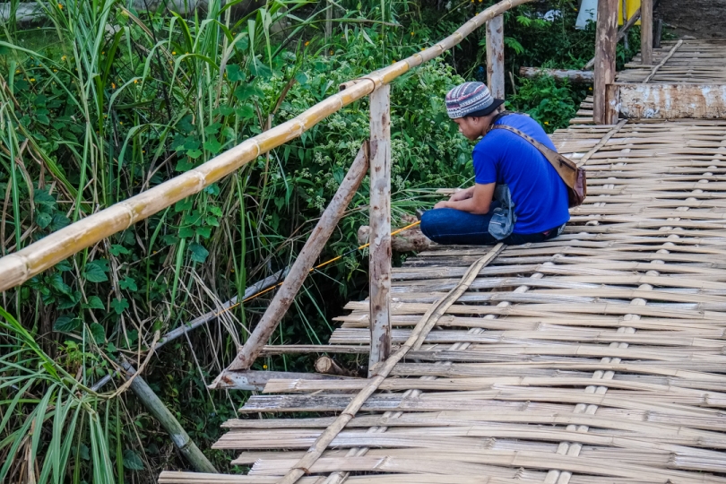 A local kid fishing from the bamboo bridge